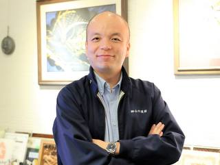 事務所で作業着姿の代表取締役 山口博康